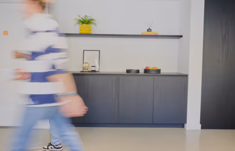 Blurred person walking past modern black cabinet with decorative items and shelf in a bright room.