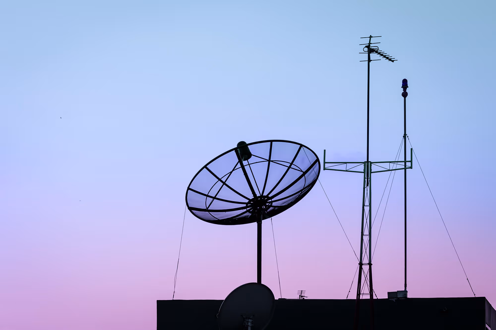 Satellite dish and antennas silhouetted against a gradient sky at dawn or dusk.