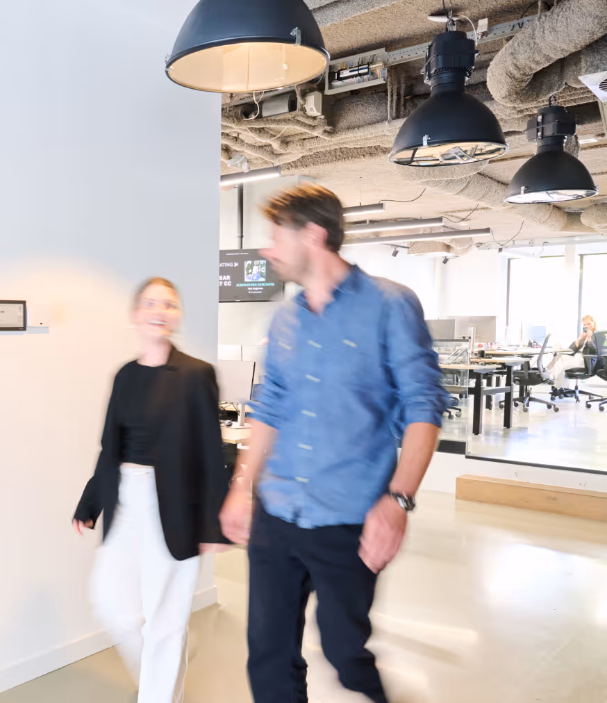 Two people walking and talking in a modern, open office with black hanging lights overhead.