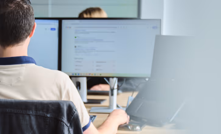 Man seated at desk working on computer with code visible on the screen.