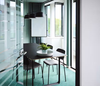 Modern conference room with black table, four chairs, green carpet, and large windows with natural light.
