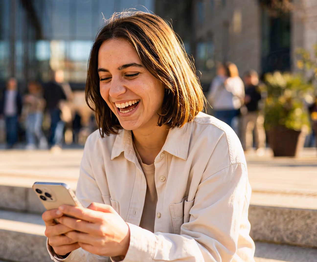 Young woman sitting outdoors on steps, smiling and looking at her smartphone.