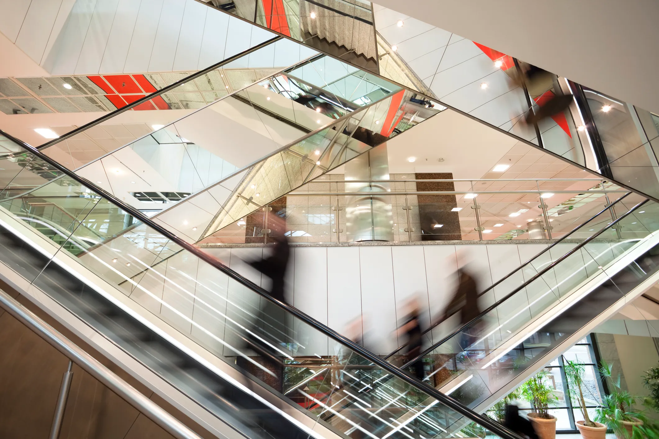 Blurred people riding escalators in a modern building with reflective glass and metal architecture.