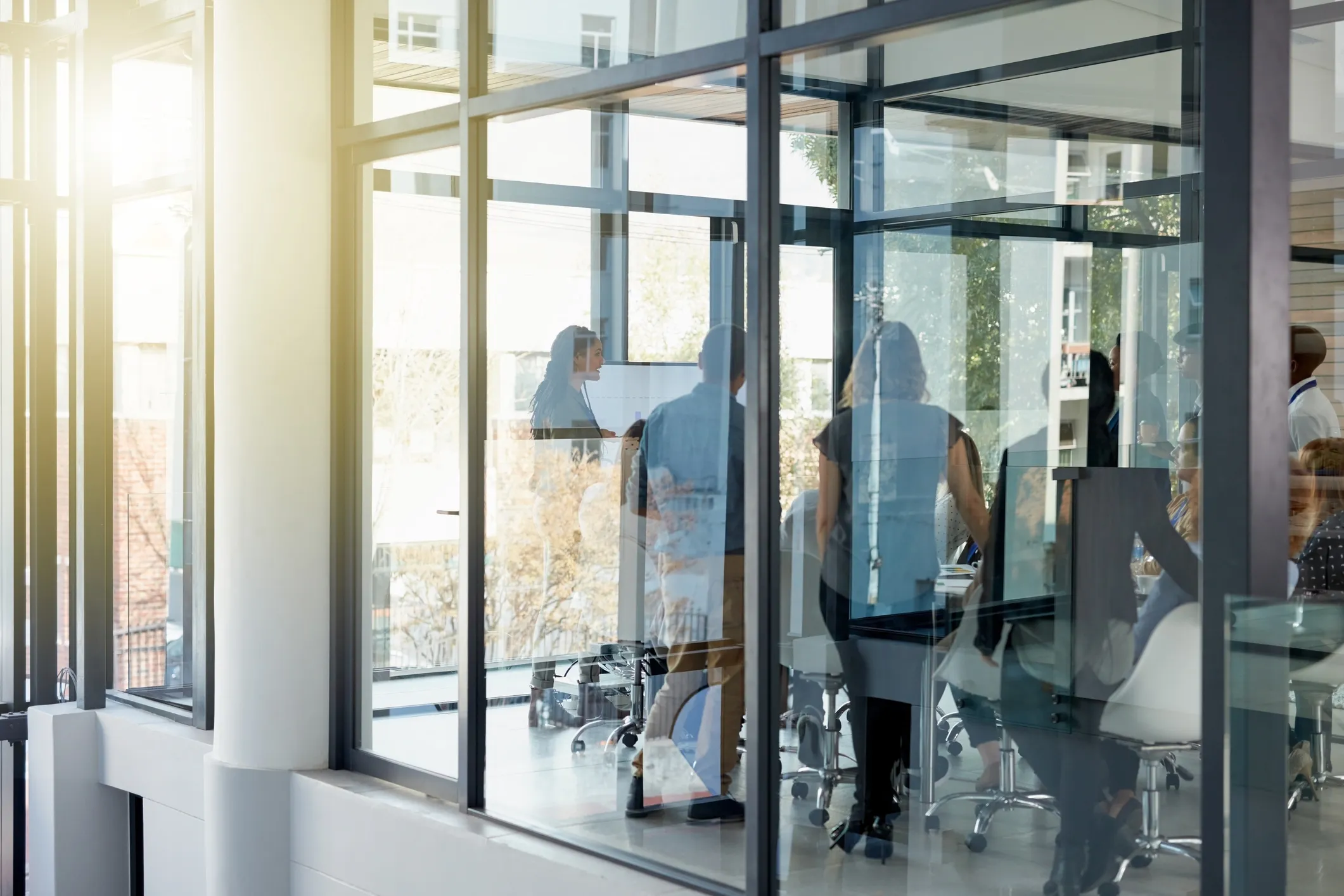 People gathered in a glass-walled office conference room during a meeting with a presenter.