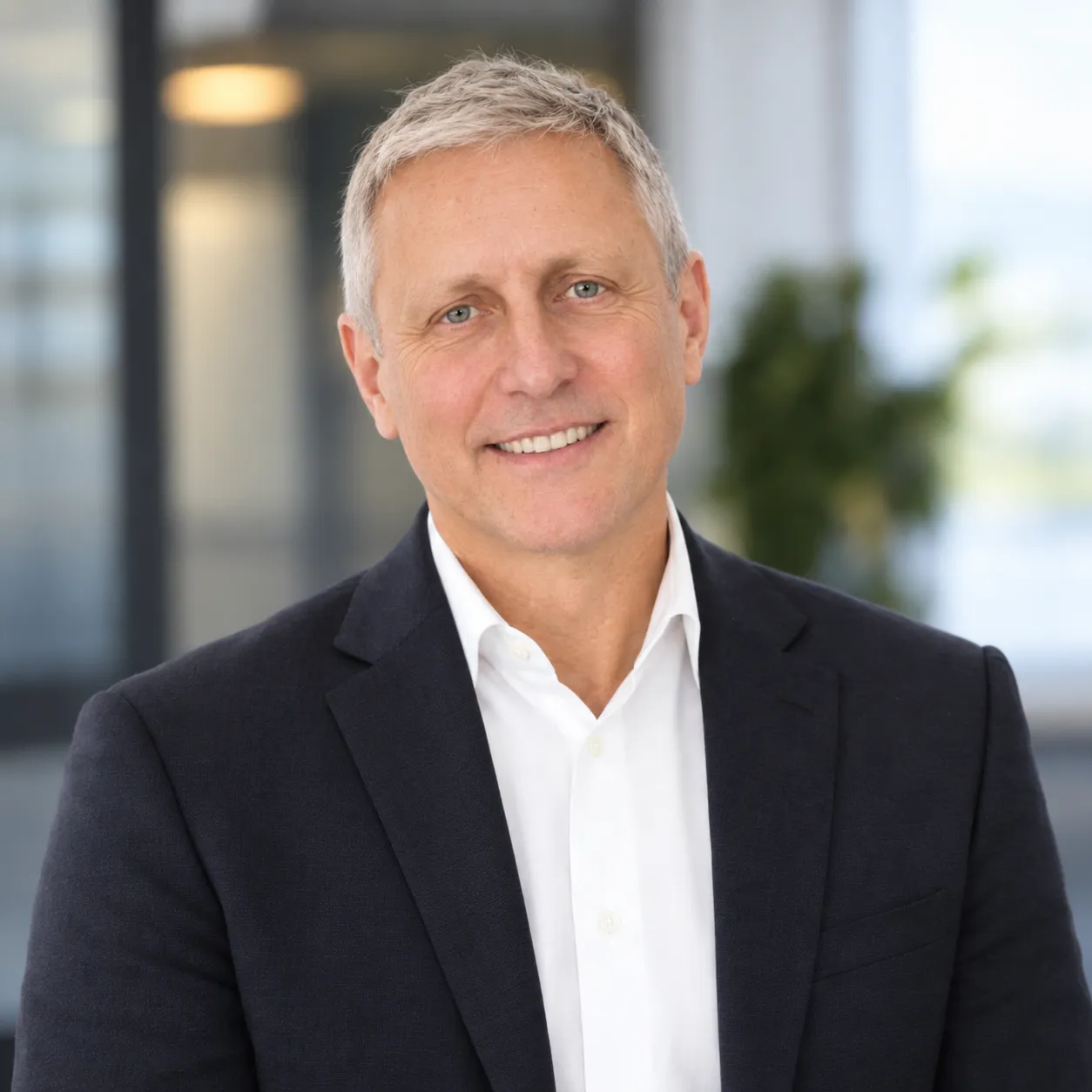 Smiling middle-aged man with gray hair wearing a dark quarter-zip sweater over a white shirt.