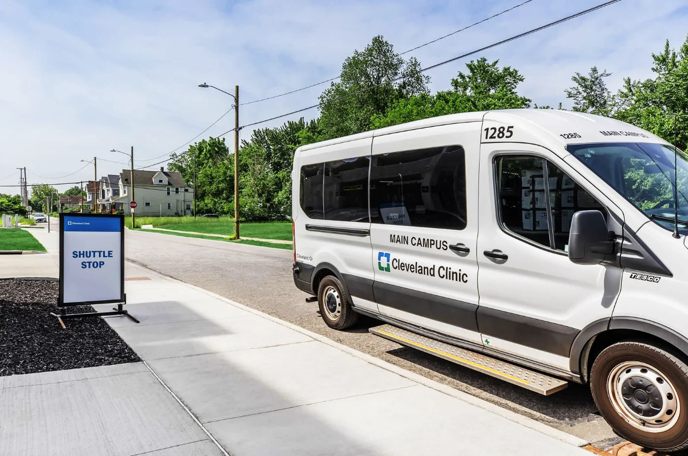 White Cleveland Clinic shuttle van parked near a sidewalk sign reading Shuttle Stop.