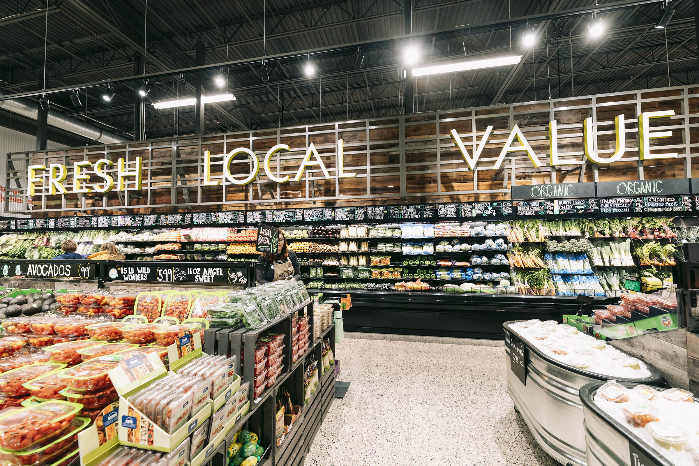 Interior of grocery store produce section with fresh vegetables, fruits, and signs reading Fresh Local Value.