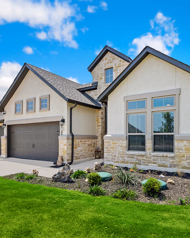 Modern house with stone and beige siding, dark garage door, windows, and landscaped front yard with green grass.