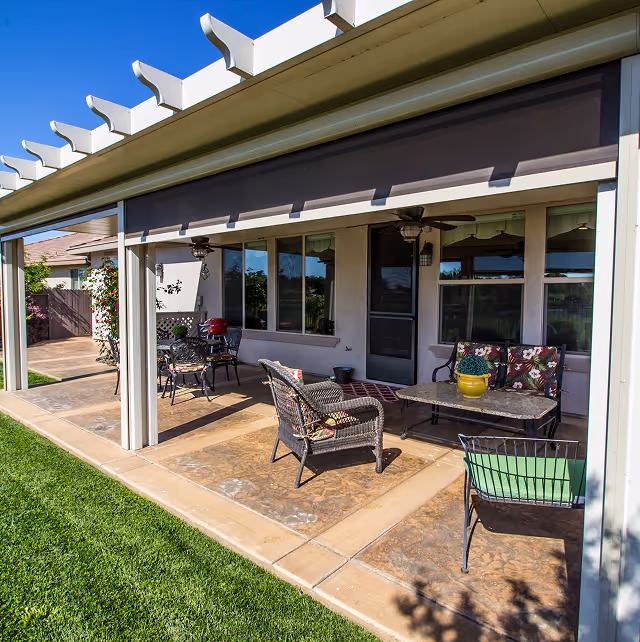 Covered patio with outdoor seating, wicker chairs, a table, and green lawn beside a house at AZ Builders.