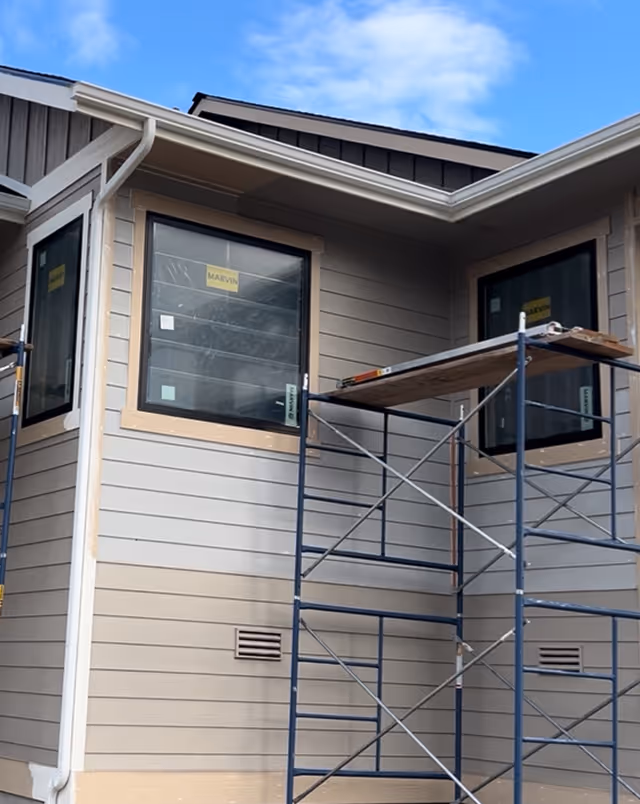 Part of a house under construction with scaffolding and three new windows installed.