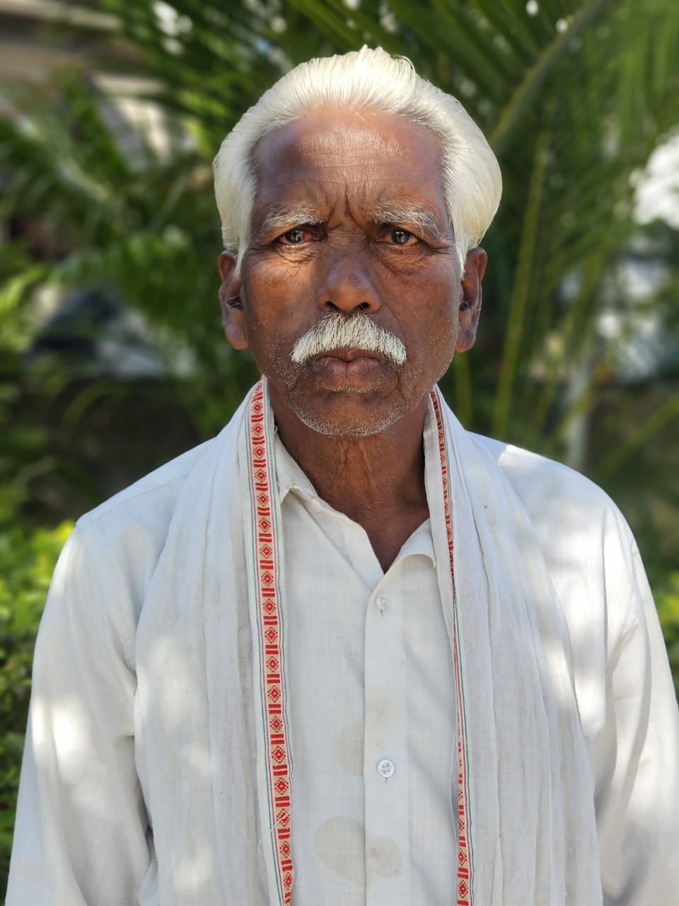 Narayan Santosh Choudhary, an elderly cotton farmer, in a white shirt and traditional shawl outdoors