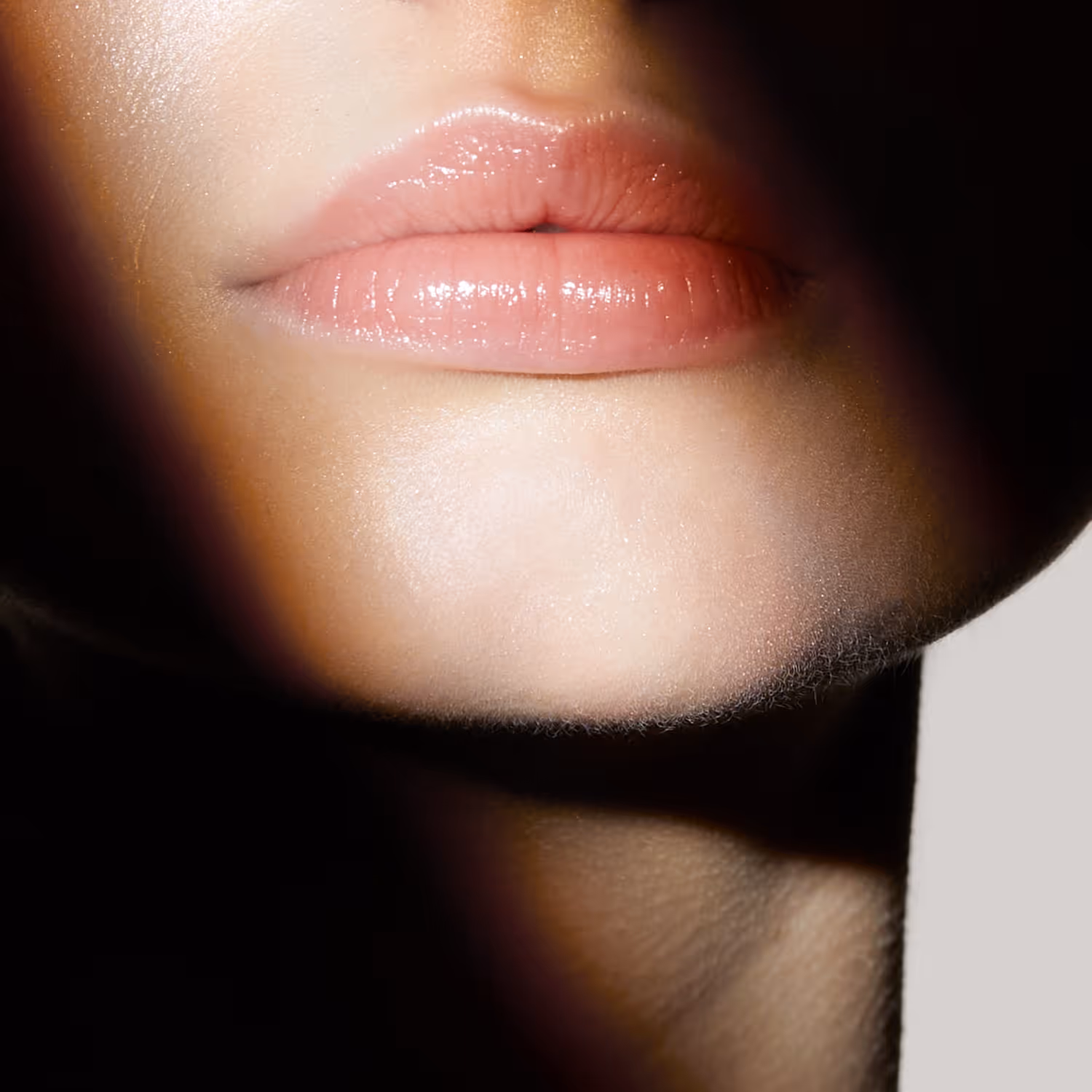 Close-up of smooth lips with glossy pink lipstick and soft lighting shadows.