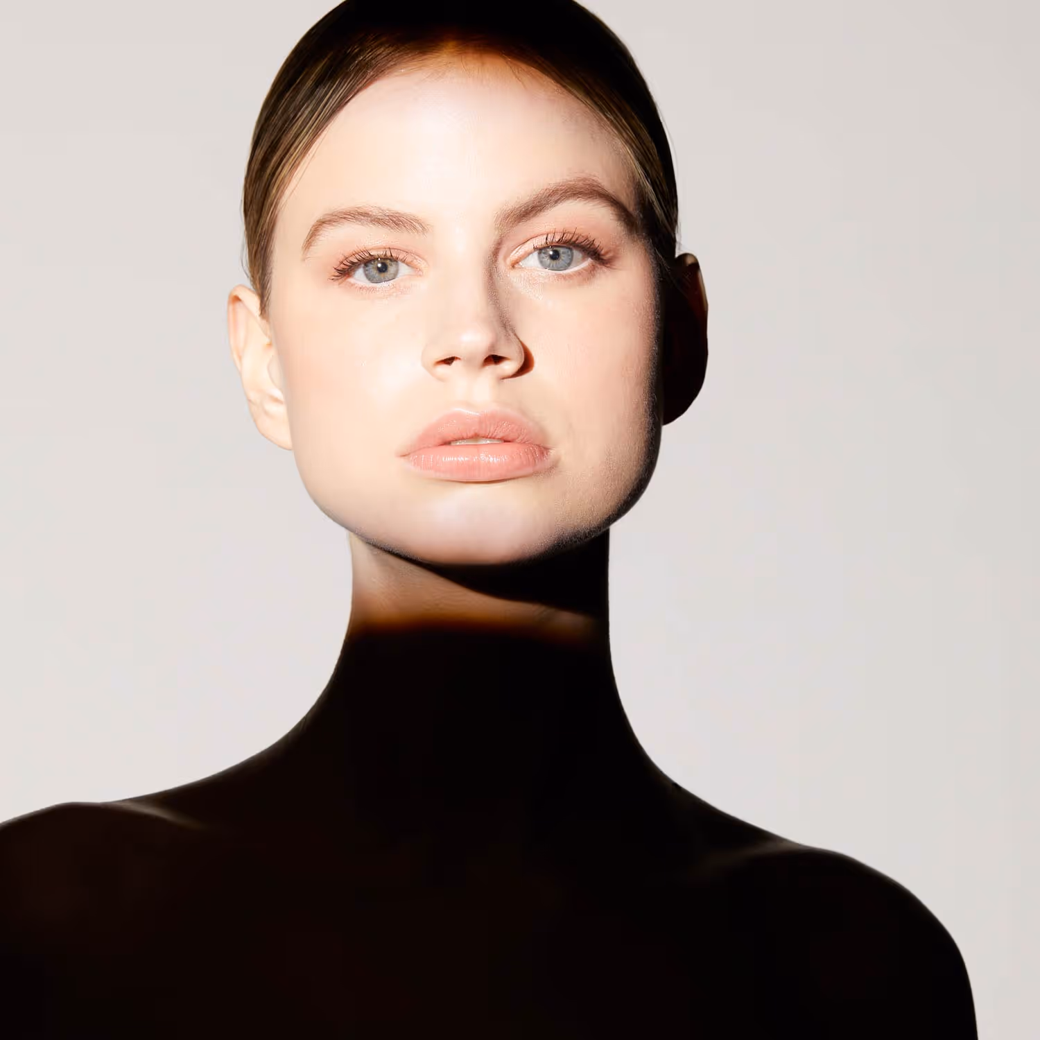 Close-up photo of a woman with blue eyes and slicked-back hair against a plain background.