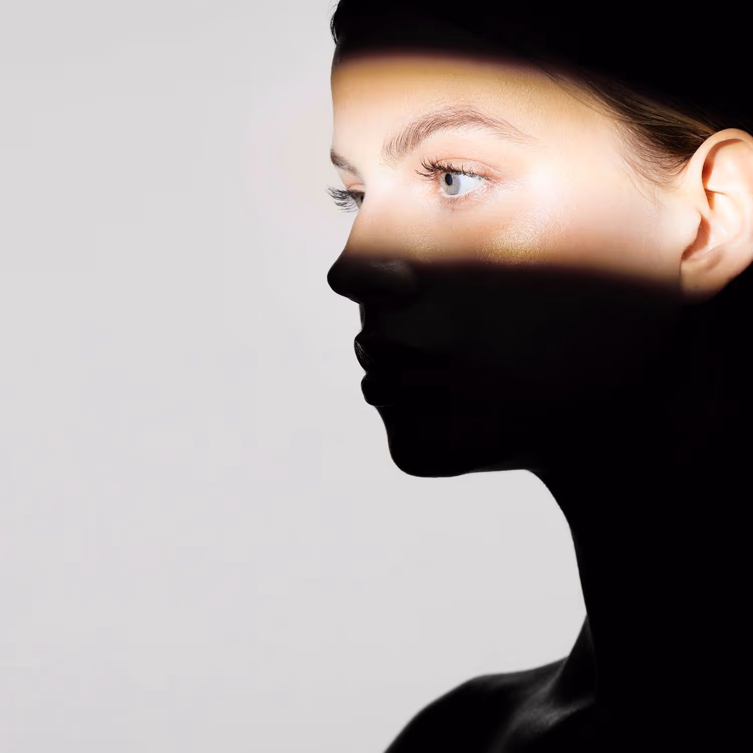 Profile of a woman with light on her eyes and forehead, rest of her face in shadow against a gray background.