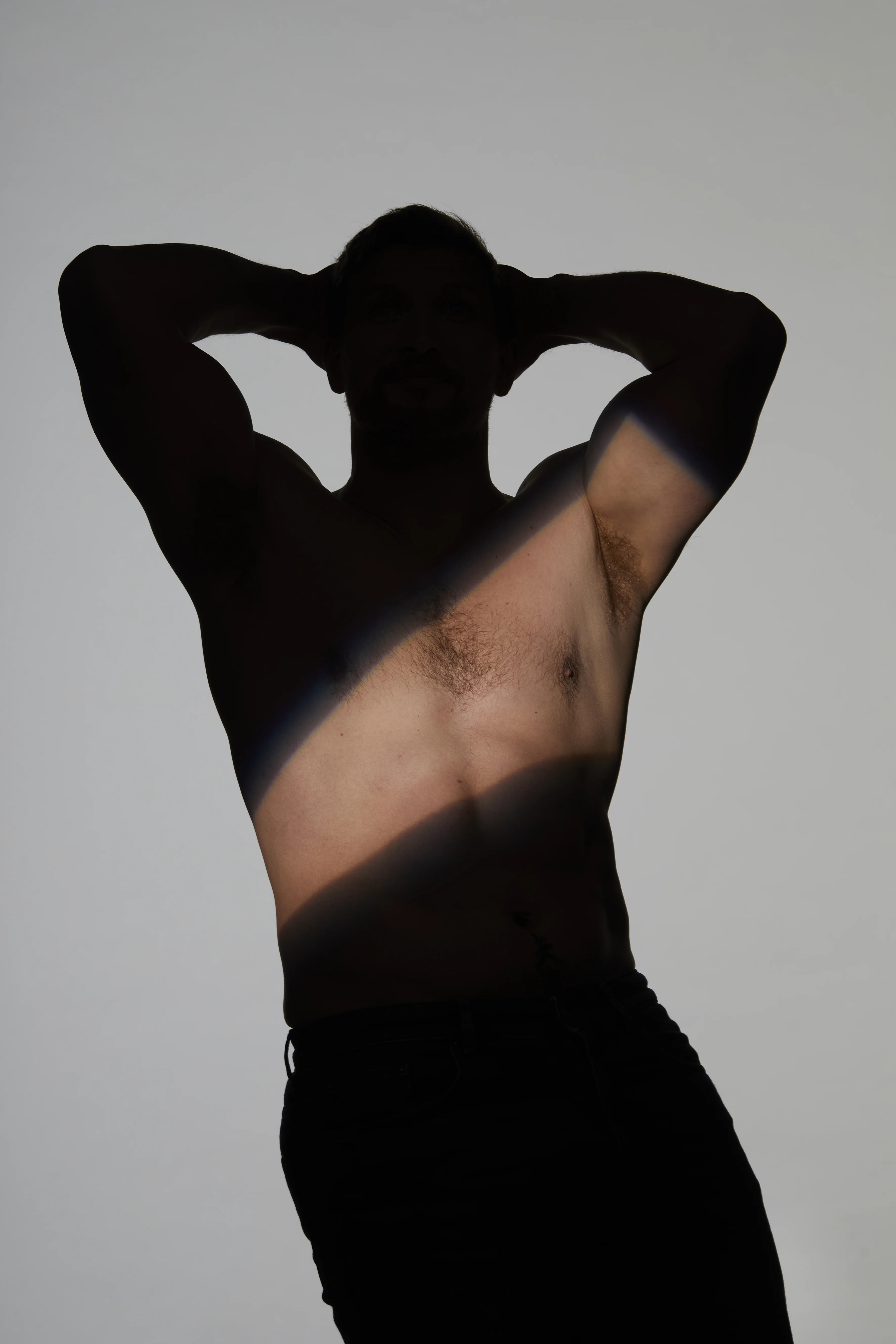 Silhouette eines Mannes mit erhobenen Armen und sichtbarer Achselpartie im Licht-Schatten-Spiel – Schweißdrüsenbehandlung München Dr. Kleeberger