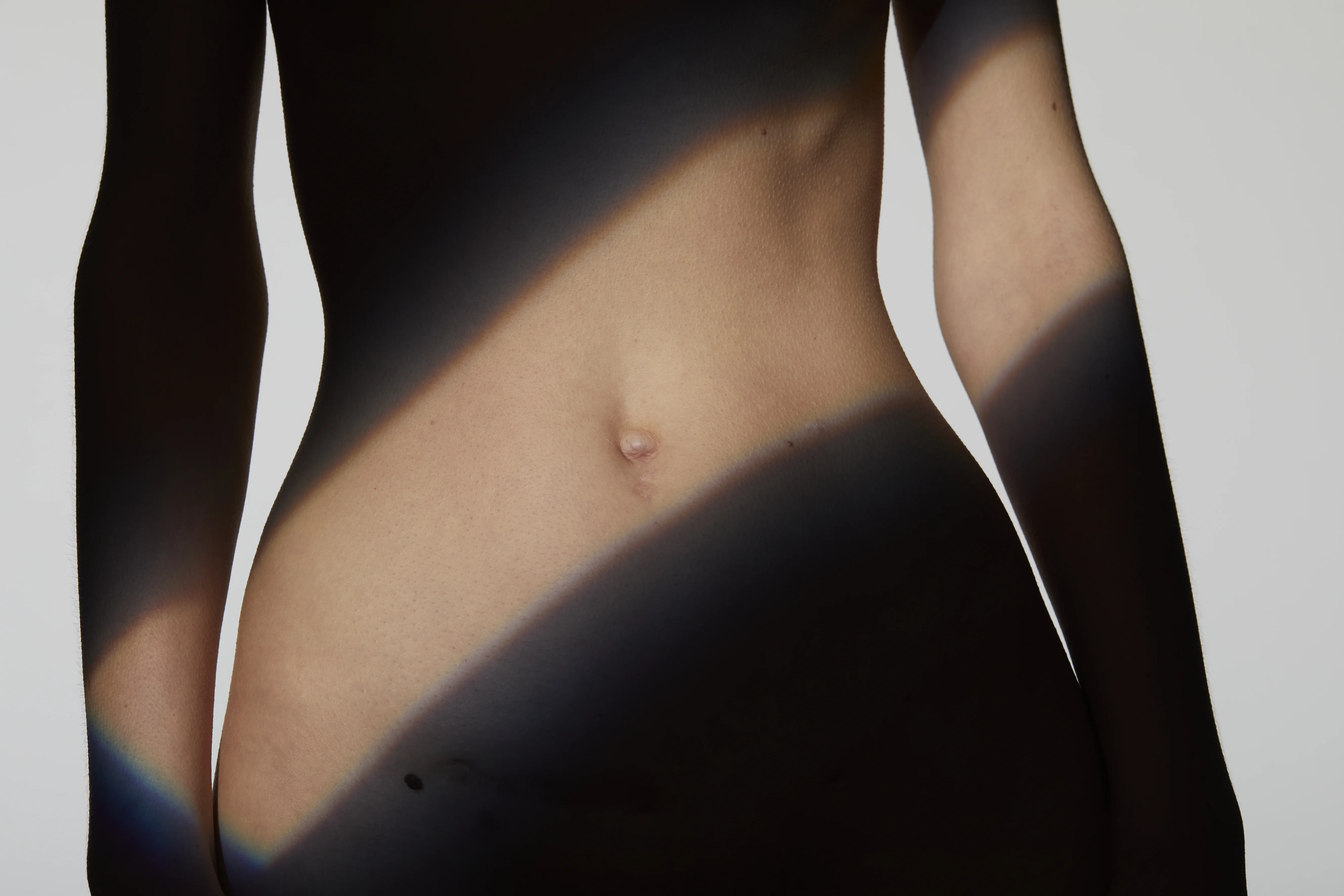 Ästhetisches Ergebnis einer Bauchdeckenstraffung (Abdominoplastik) am flachen Bauch einer Frau, kunstvoll inszeniert mit Licht und Schatten.