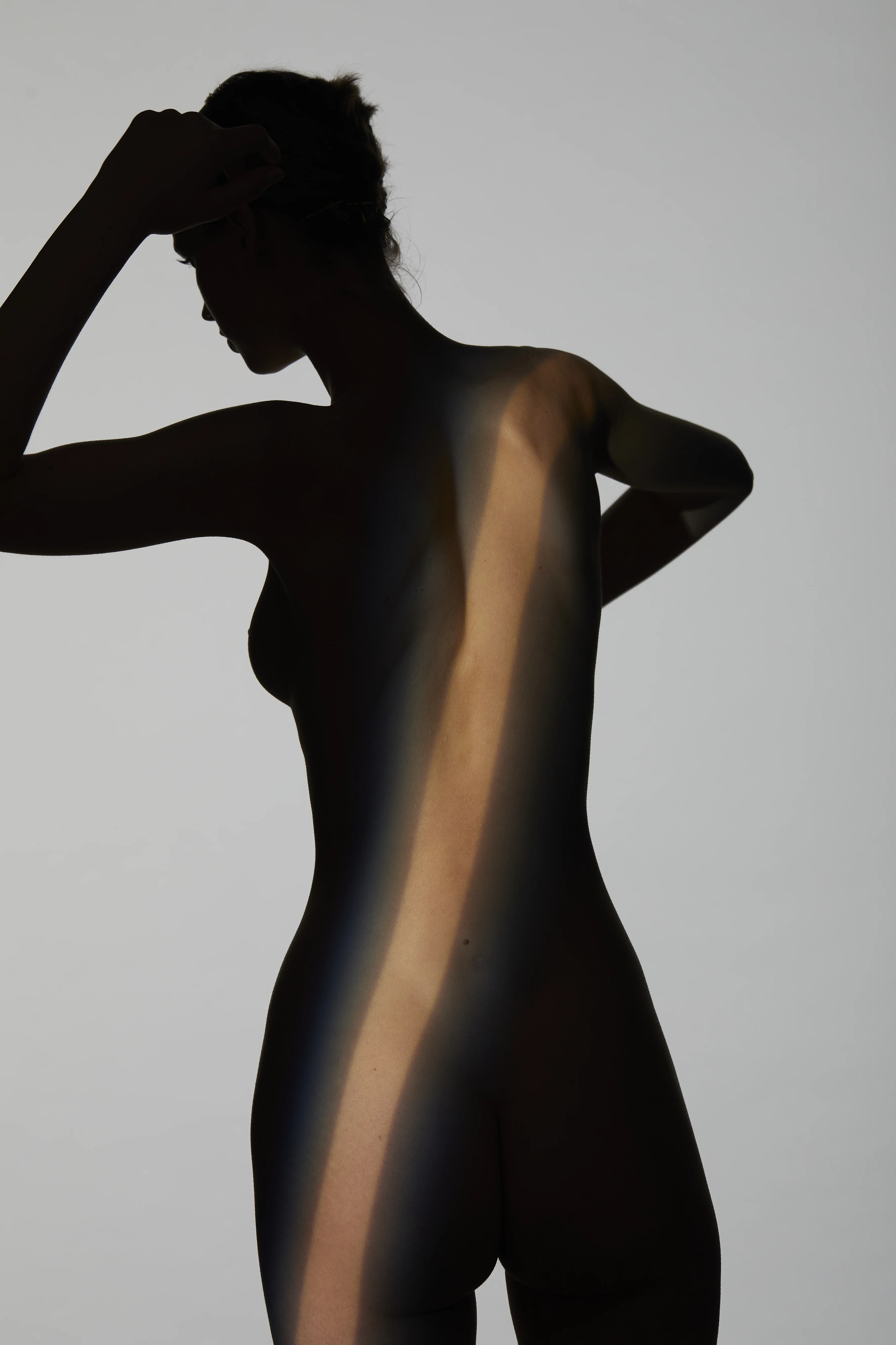 Künstlerische Silhouette einer weiblichen Silhouette im Profil mit Fokus auf die geschwungene Linie von Taille und Hüfte nach einem Bodylift, betont durch einen diagonalen Lichtstrahl.