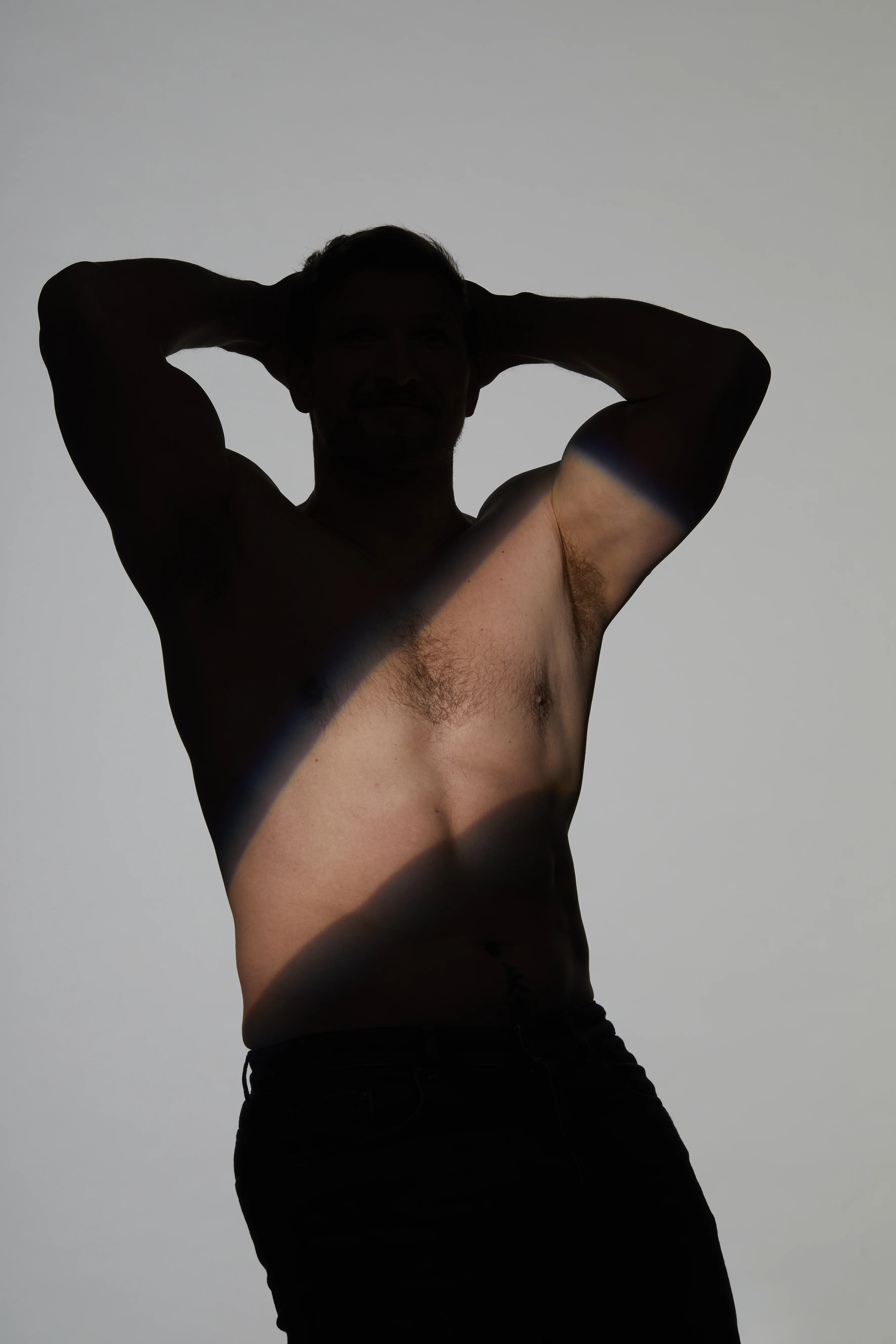 Ästhetische Aufnahme eines Mannes mit hinter dem Kopf verschränkten Armen und freier Achselpartie, akzentuiert durch Licht und Schatten – passend zum Thema Schweißdrüsenbehandlung gegen übermäßiges Schwitzen (Hyperhidrose).