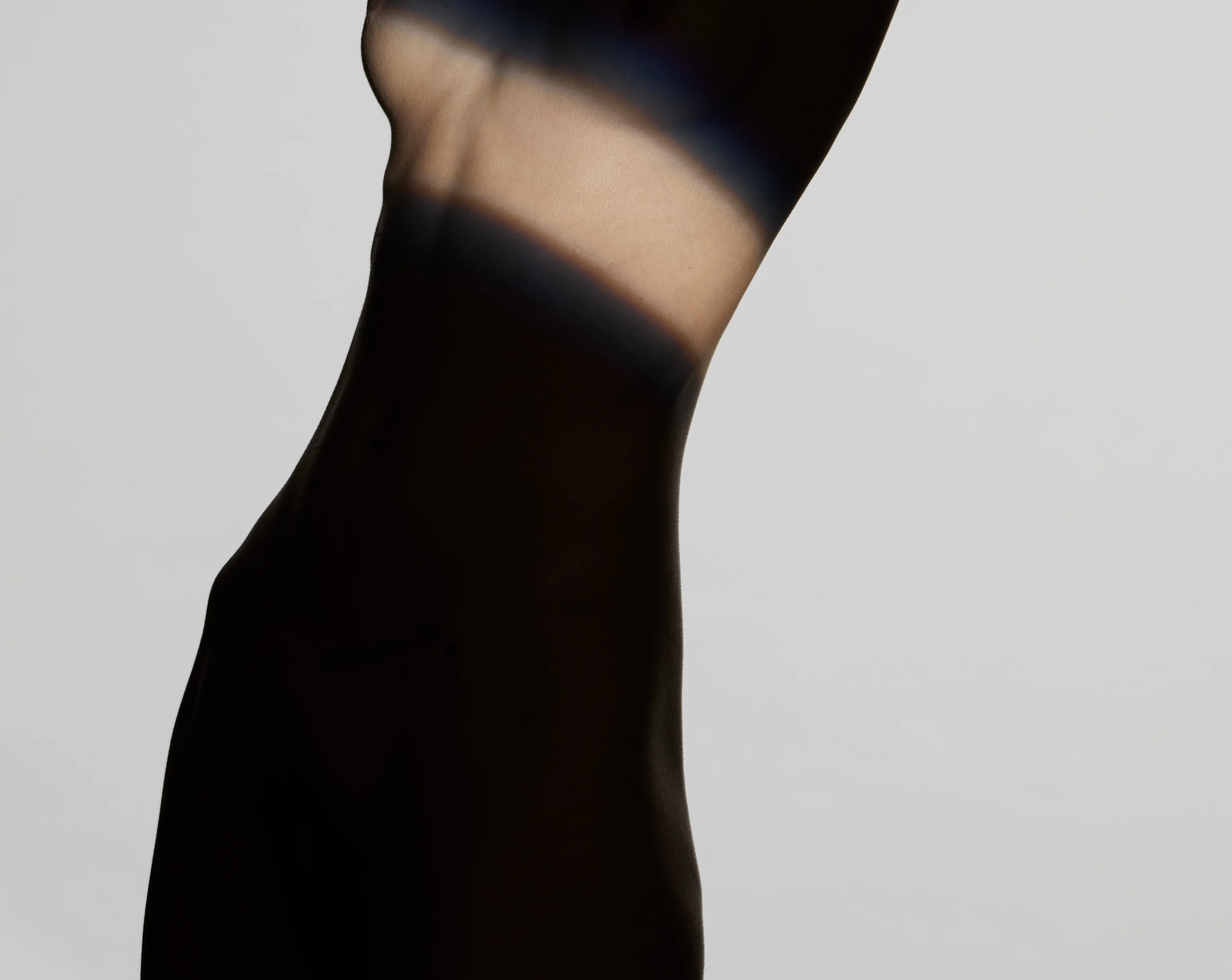 Ästhetische Silhouette eines weiblichen Torsos in der Seitenansicht vor hellem Hintergrund, bei der ein gezielter Lichtstreifen die Brust- und Dekolleté-Partie betont – zur Veranschaulichung einer Bruststraffung oder ästhetischen Brustkorrektur.