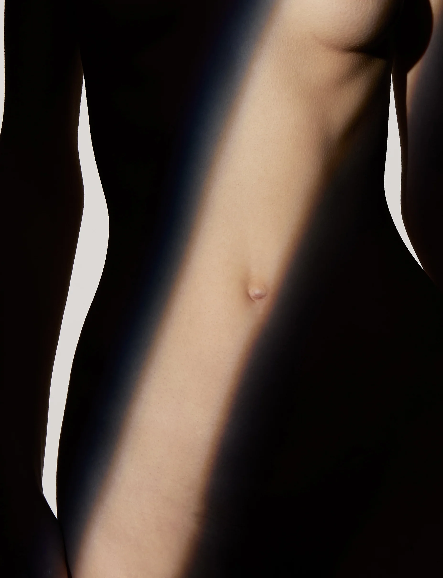 Ästhetische Detailaufnahme eines weiblichen Oberkörpers mit Fokus auf die Bauch- und Brustpartie, bei der ein diagonaler Lichtstrahl die Konturen hervorhebt – zur Veranschaulichung einer Brustkorrektur bei Brustasymmetrie.