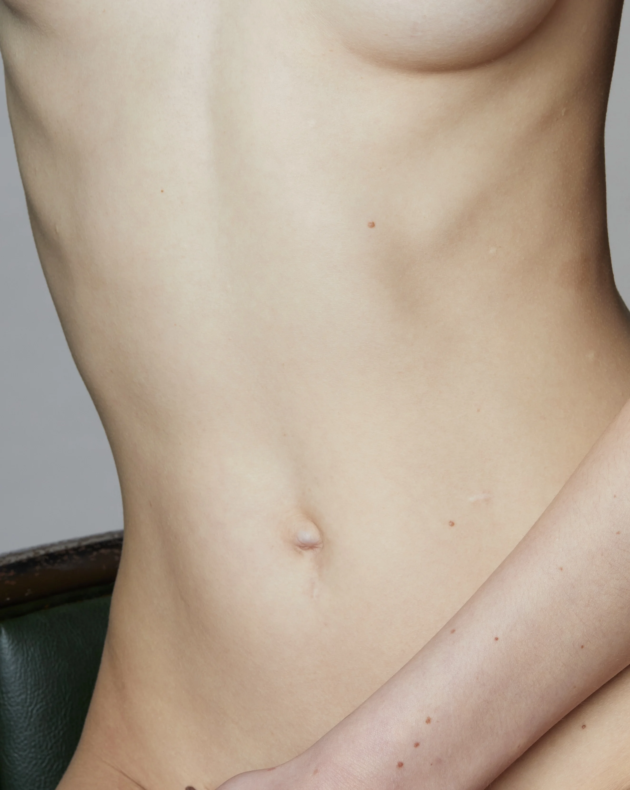 Ästhetische Detailaufnahme eines weiblichen Torsos von der Seite im Sitzen mit Fokus auf die Bauch- und Unterbrustpartie – zur Veranschaulichung einer operativen Korrektur bei Brustasymmetrie.