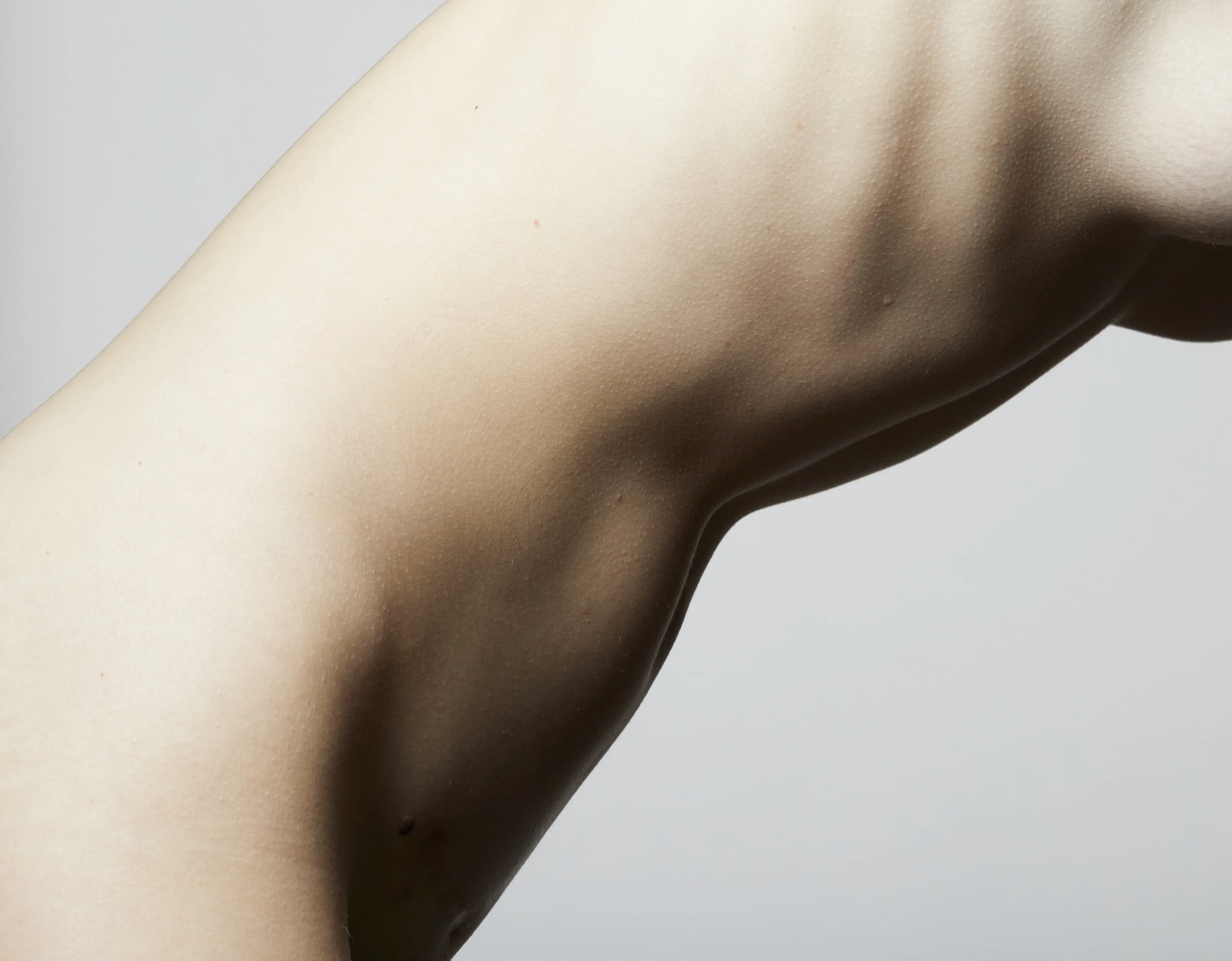 Ästhetische Nahaufnahme eines Torsos von der Seite vor hellem Hintergrund mit Fokus auf die Rippenbogen- und Unterbrustpartie – zur visuellen Unterstützung für eine Schlupfwarzenkorrektur oder ästhetische Brustbehandlungen.