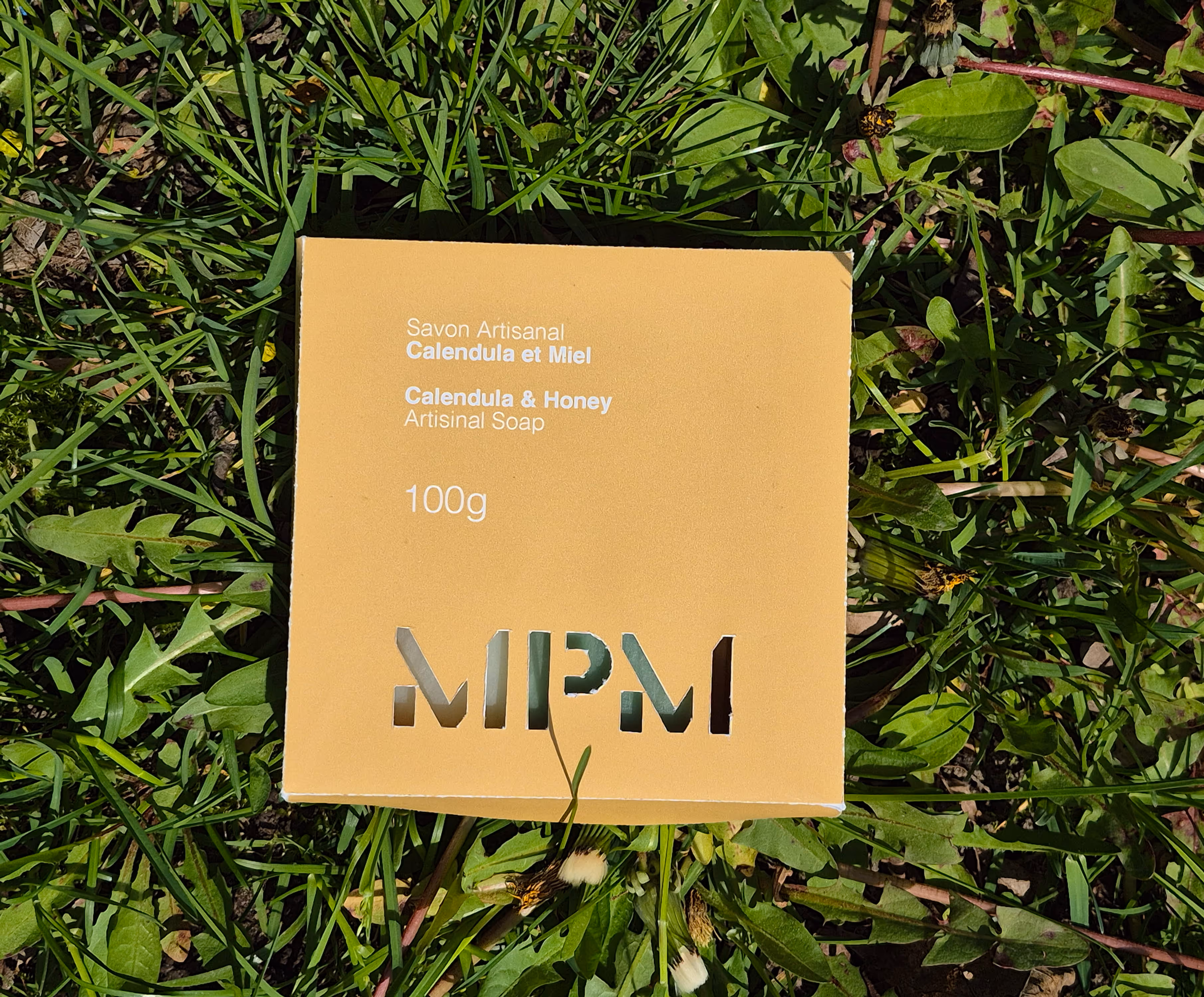 Yellow box of artisanal calendula and honey soap weighing 100g on grass.