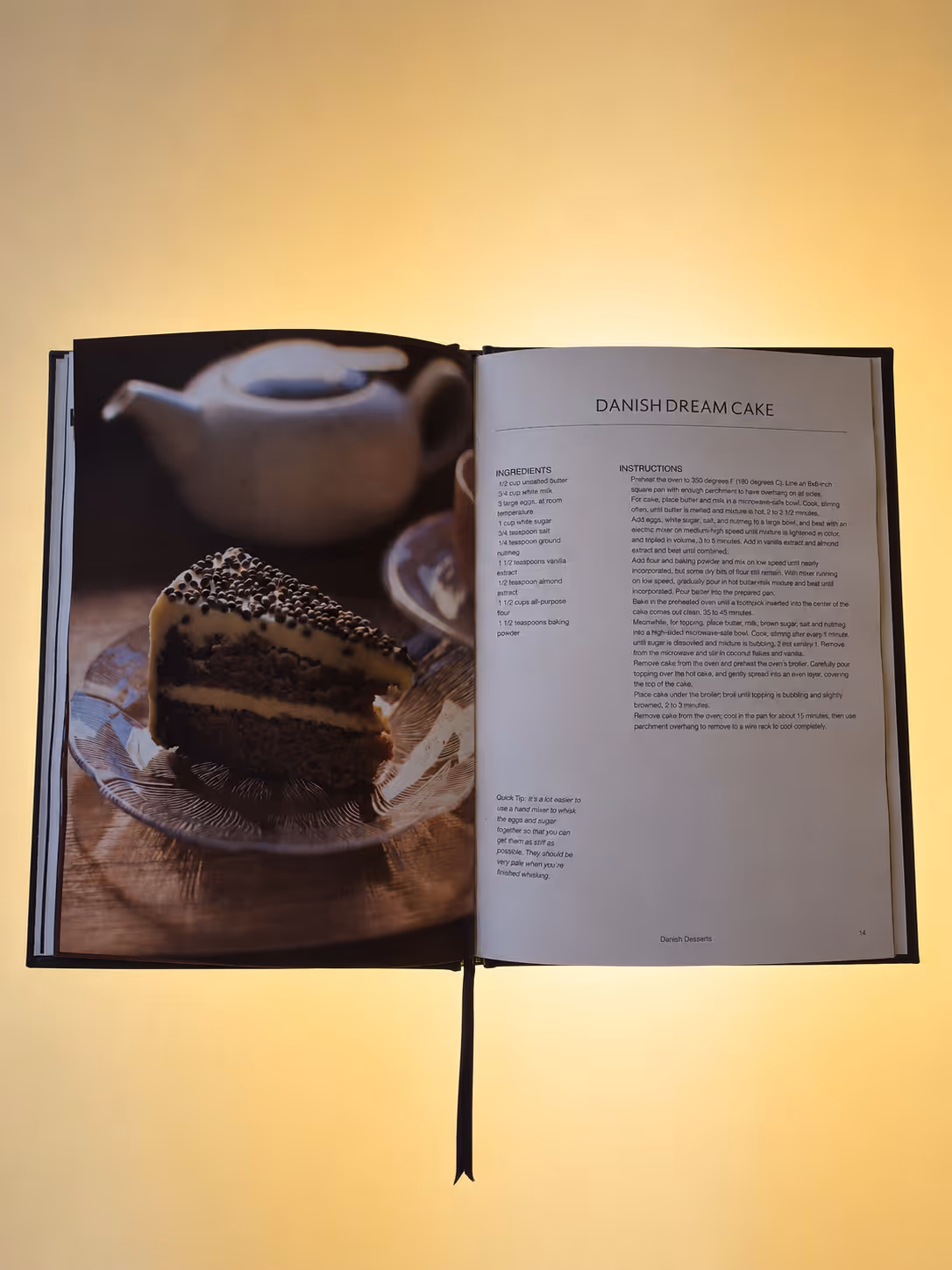 Open book showing Danish Dream Cake recipe with a photo of a slice of cake on a plate with a teapot.