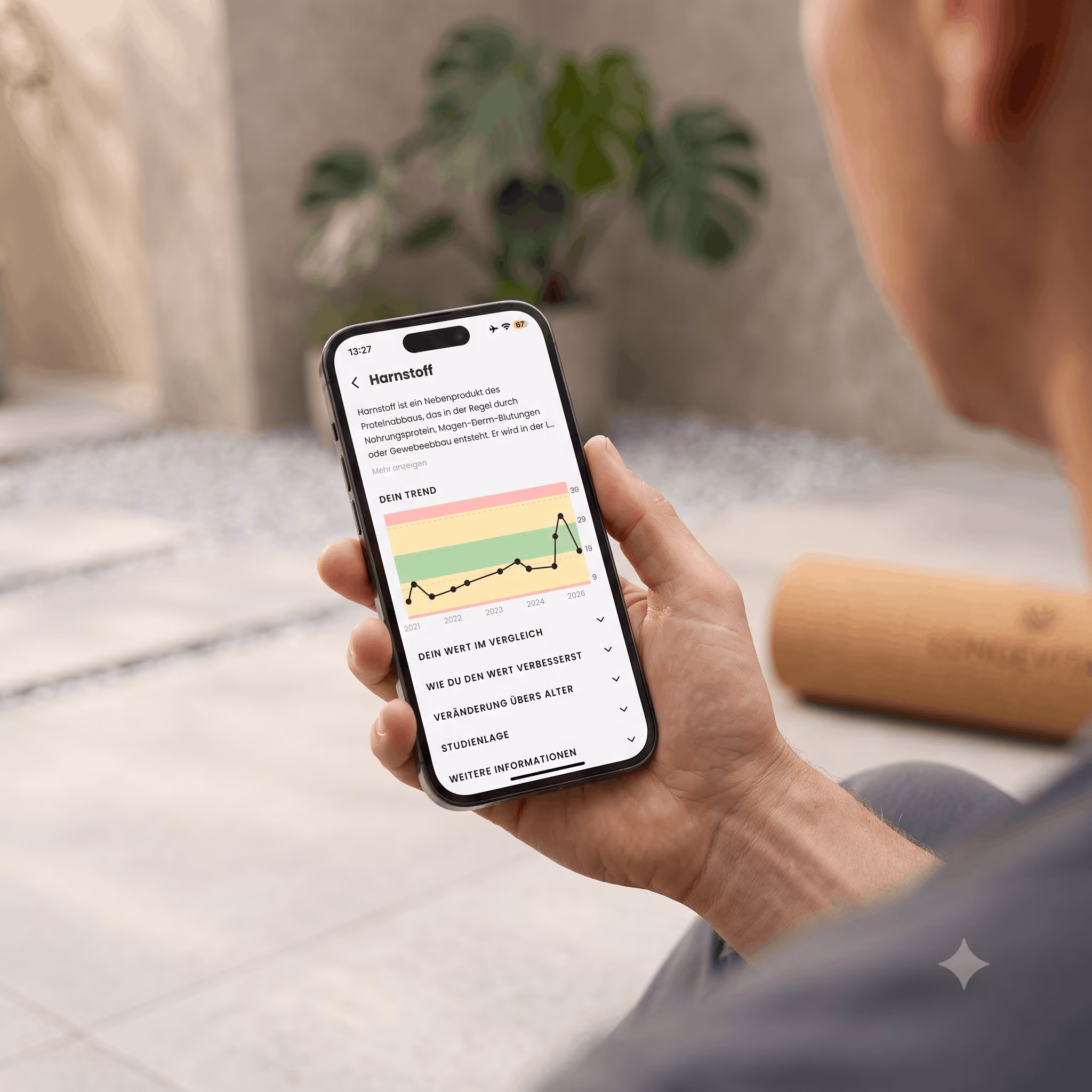 Eine Person hält ein Smartphone mit einer Anzeige zur Harnstoff-Trendkurve von 2021 bis 2026 in einer App.