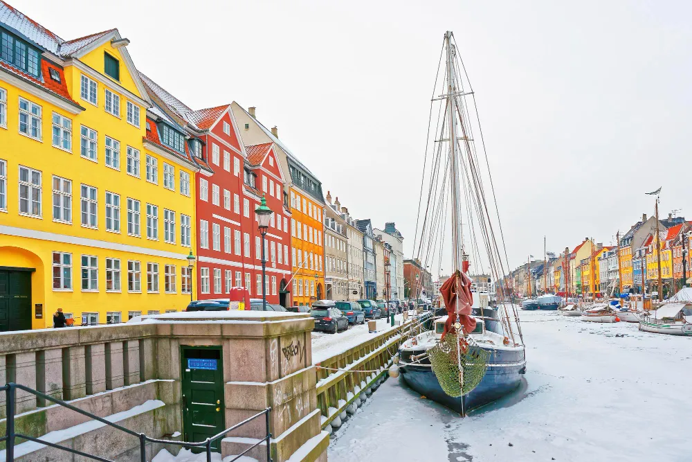 Nyhavn canal in Copenhagen with colourful houses and a moored boat in snow