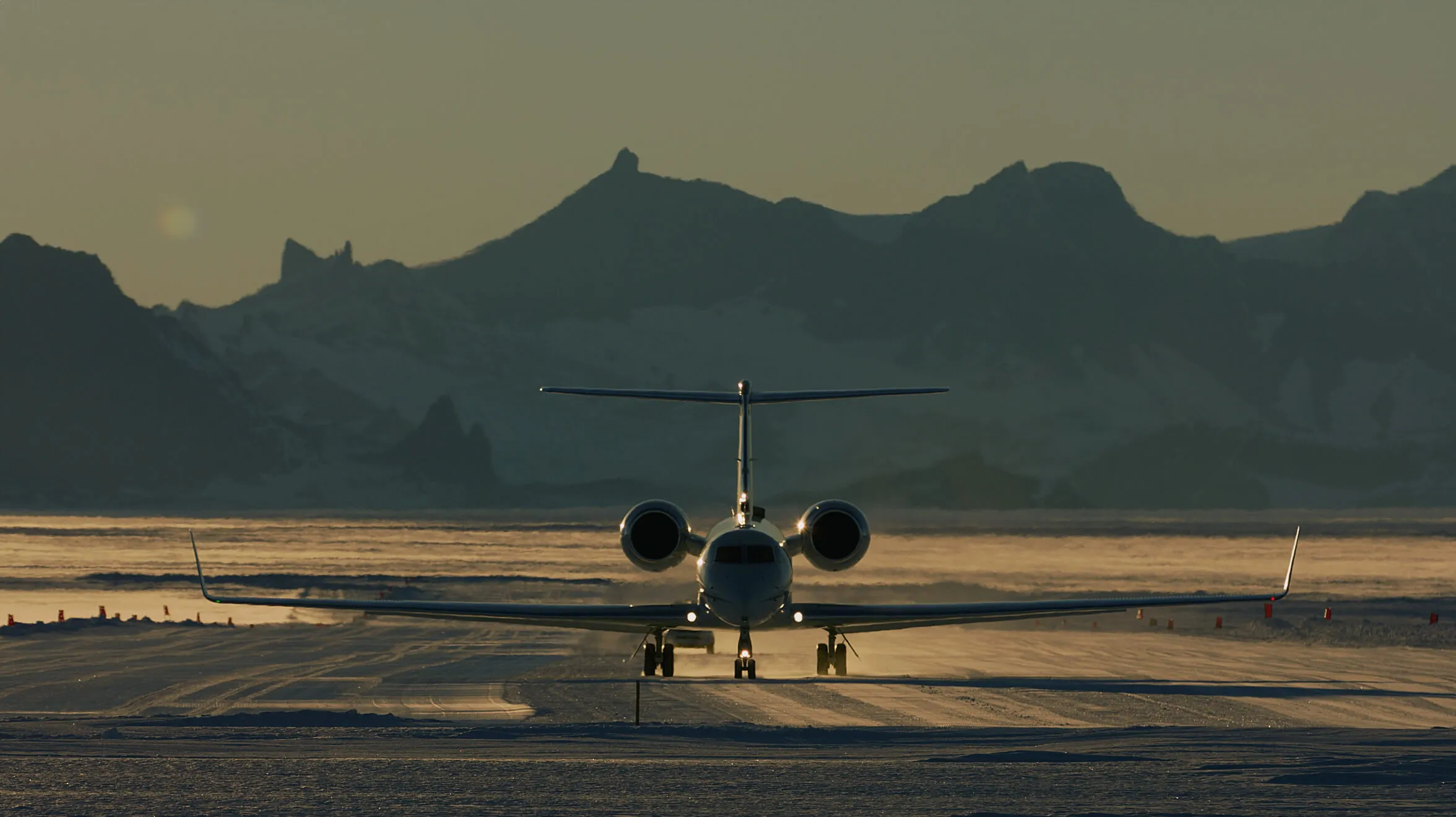 Business jet on a snowy runway at dusk with mountains behind