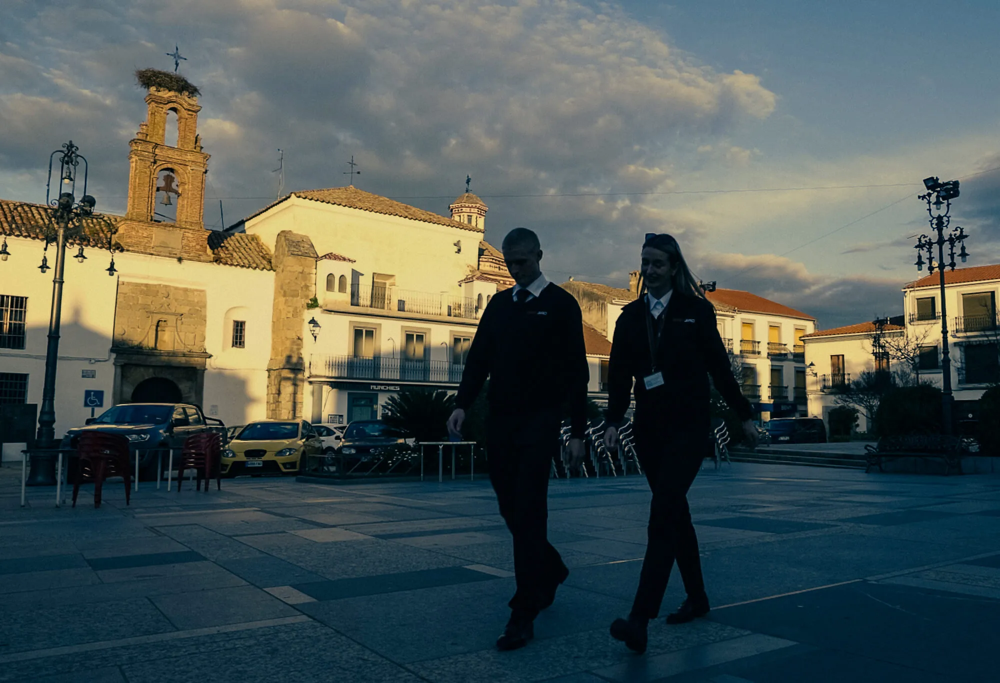 Two Greybird students in uniform walking through a Spanish town square at sunset