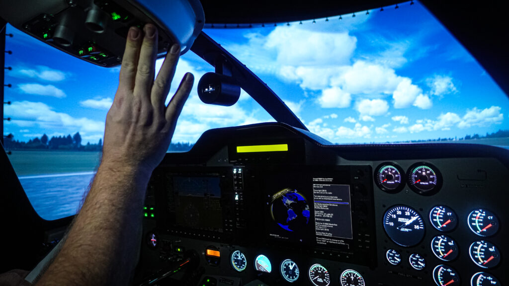 Pilot's hand on the overhead panel inside an FNPT II simulator cockpit