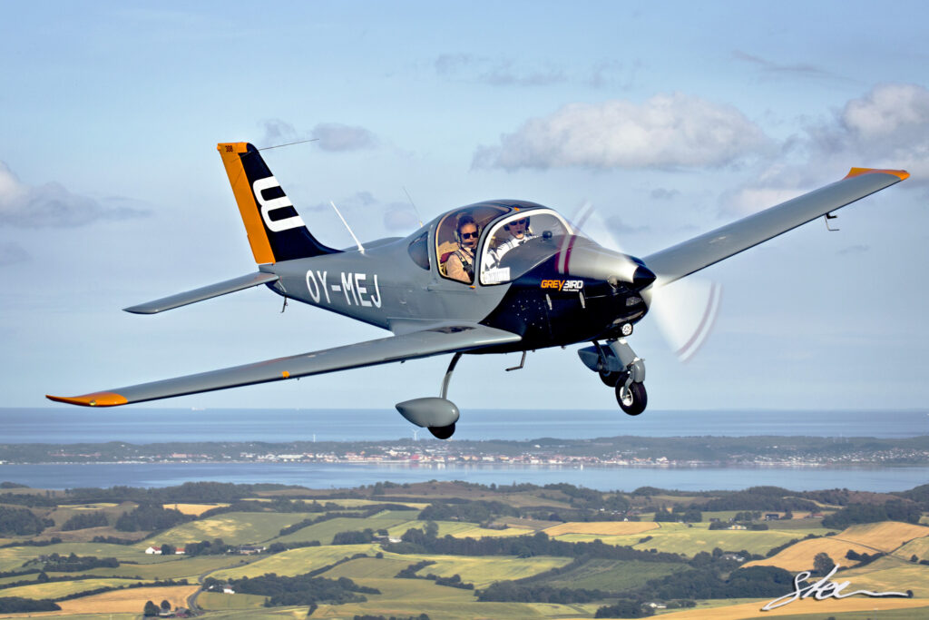 Single-engine Tecnam P2002JF Greybird aircraft in flight over coastline