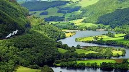 Green valley with a winding river and hills covered in dense forest and grassy fields.