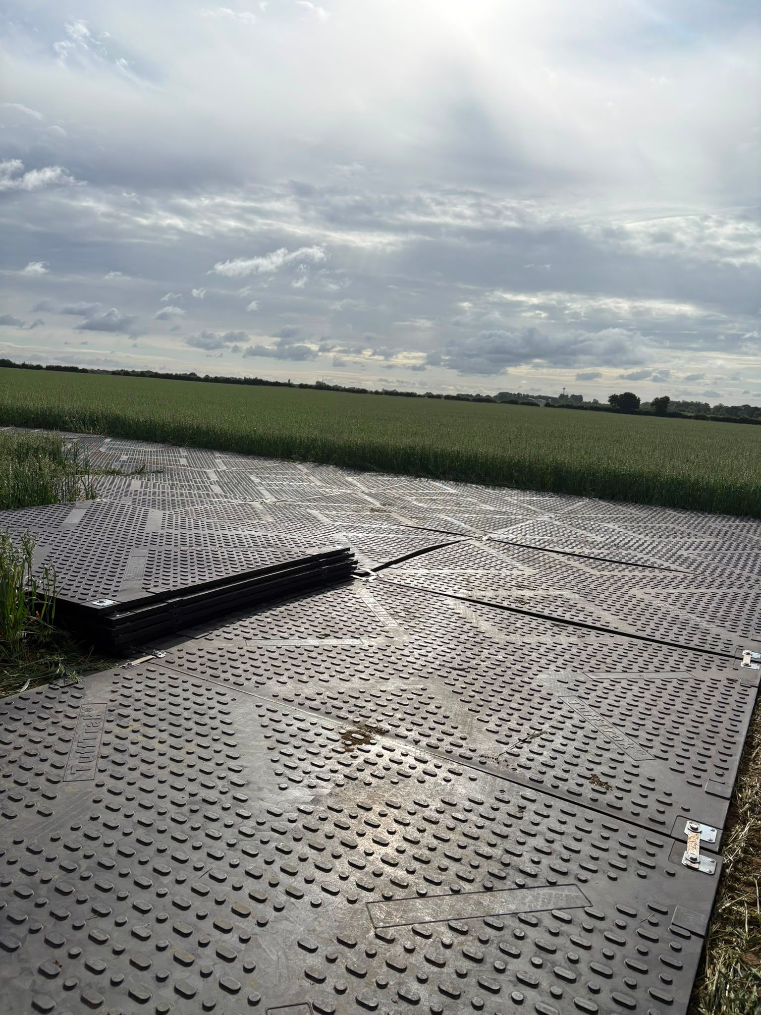 Multiple stacks of ground protection mats ready for deployment on a grassy field, demonstrating scale and logistics.