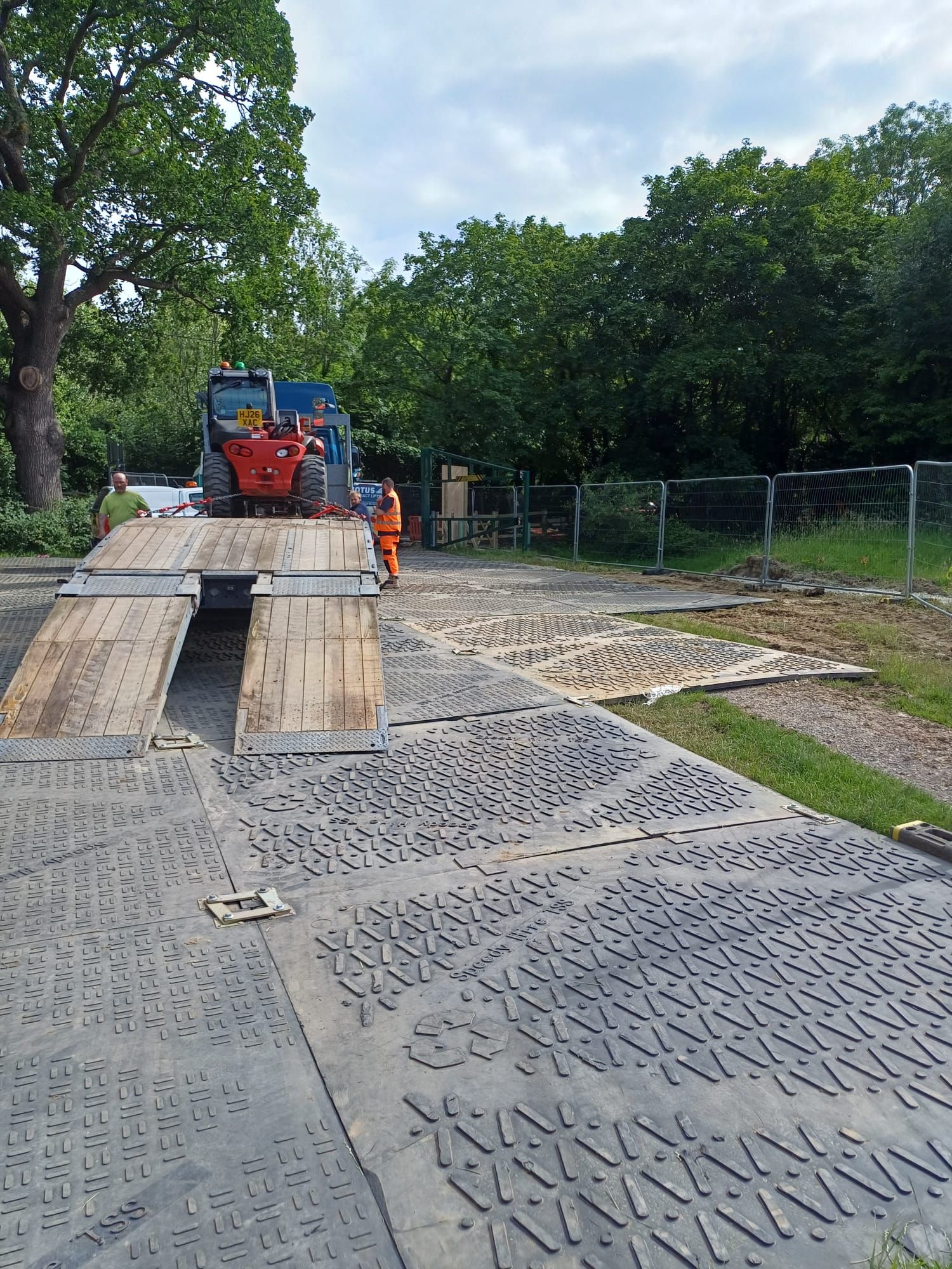A long stretch of heavy-duty ground protection mats installed across a grassy field to provide safe access for vehicles and pedestrians while protecting the underlying turf.