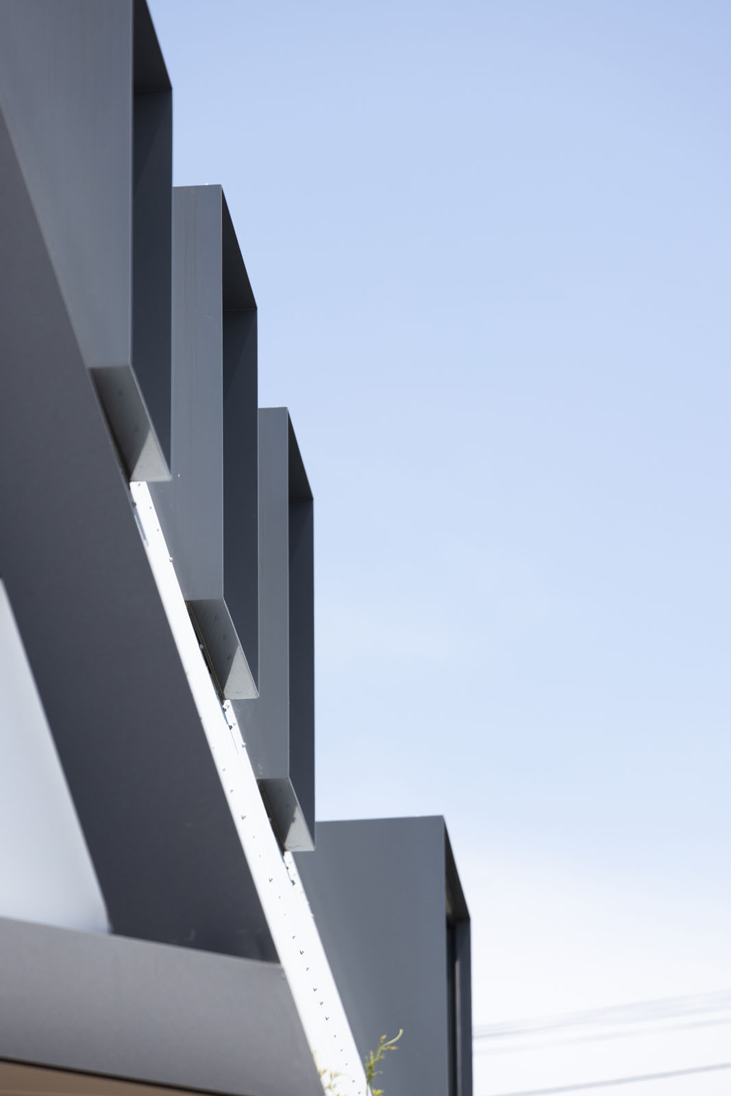 Close-up of a modern building facade featuring dark gray rectangular architectural elements protruding vertically against a clear blue sky.