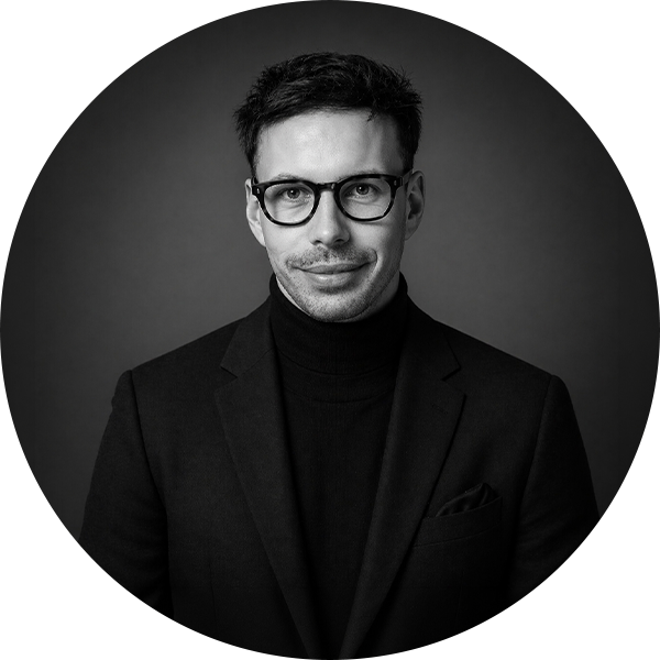 Black and white portrait of a man wearing glasses, a turtleneck, and a blazer, smiling slightly.