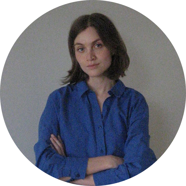Woman with short brown hair wearing a blue button-up shirt, arms crossed, neutral expression.