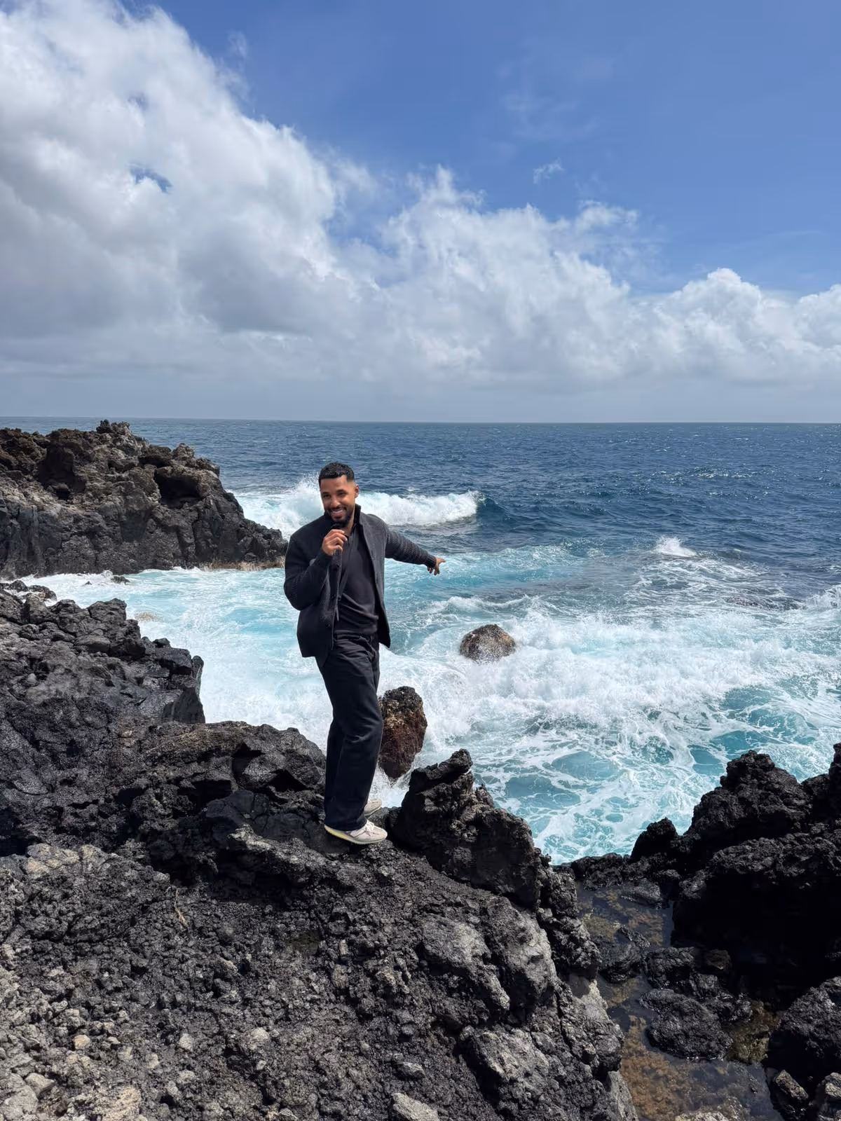 David Kwasi Owusu auf Lavafelsen am Meer – Retreat Outdoor Foto in dunklem Outfit mit weißen Sneakern
