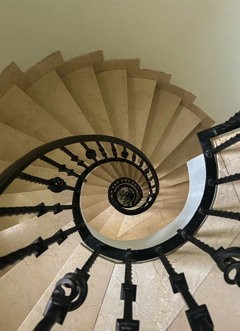 Spiralförmige Treppe aus Stein mit schwarzem Geländer von oben gesehen.