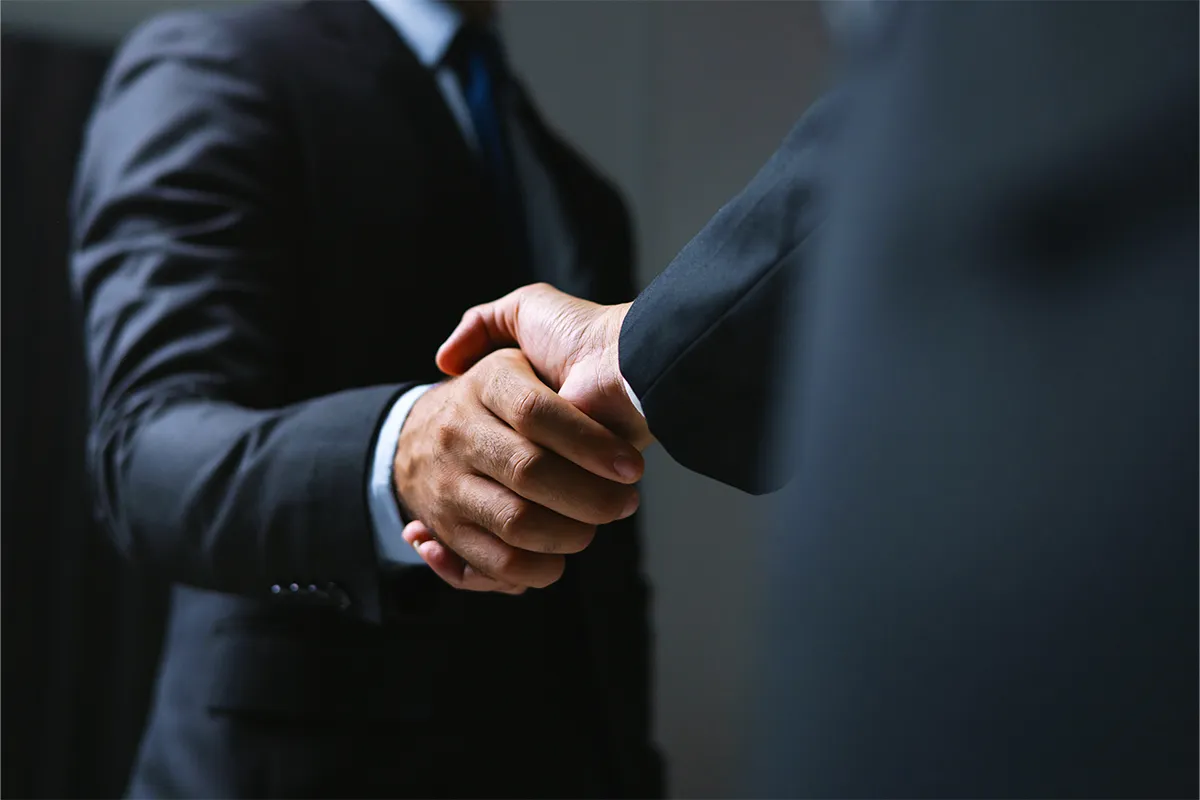 Zwei Geschäftsmänner geben sich in Anzügen die Hand zum Handschlag.