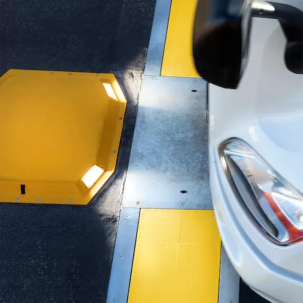 White car driving through a WheelRight tyre inspection system with yellow reflective panels on black asphalt.