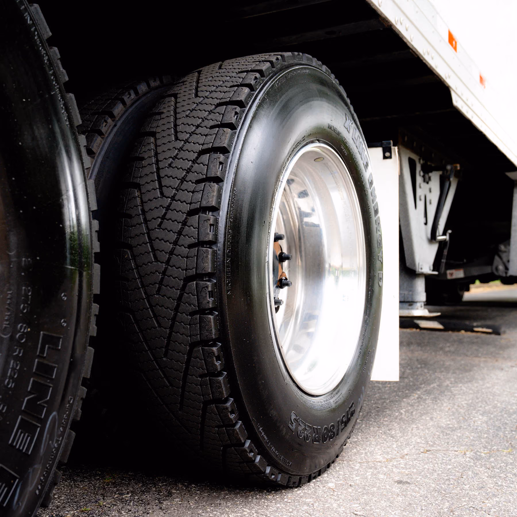 Close-up of two Michelin truck tires on the rear axle of a trailer on paved ground.