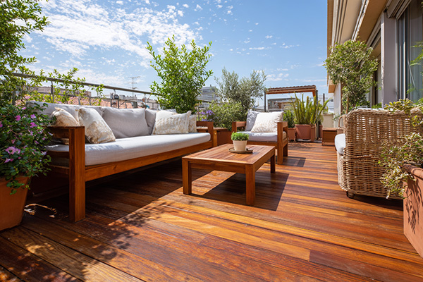 Wooden patio deck with cushioned sofas, coffee table, and potted plants under a blue sky.