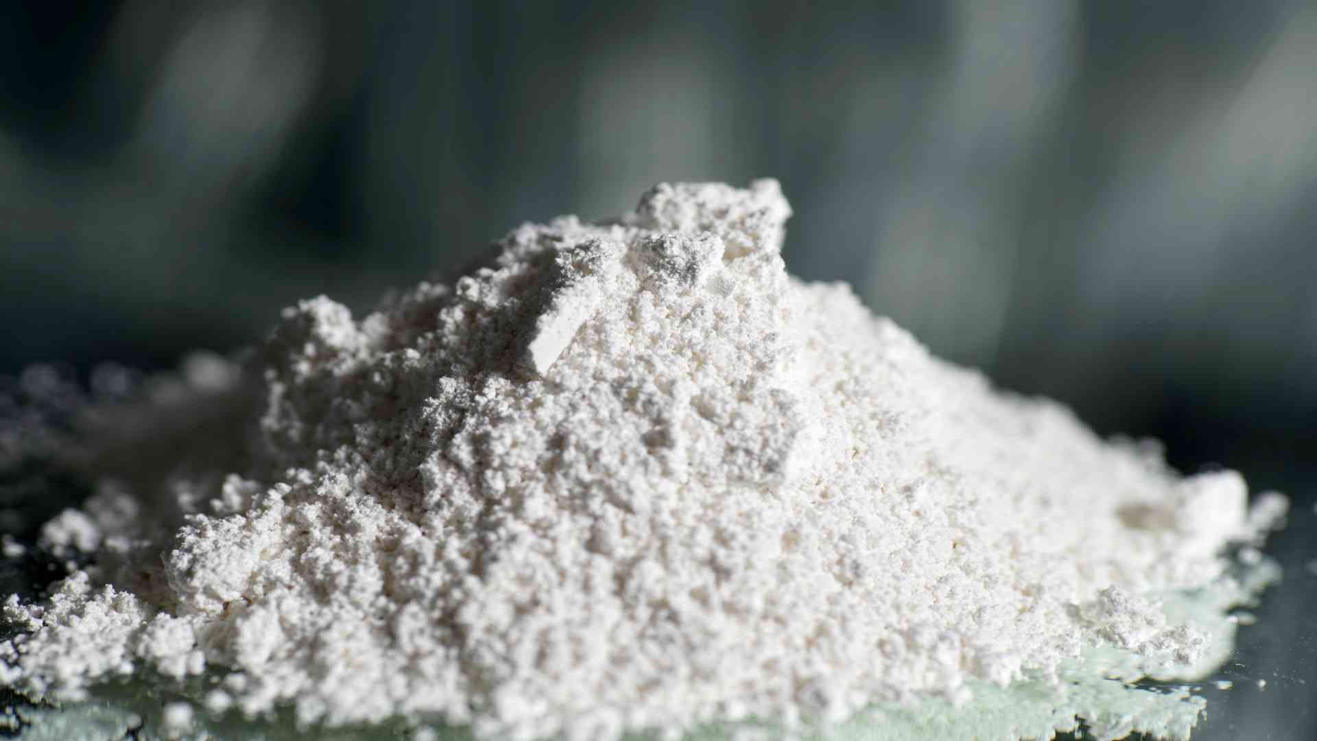 Close-up of a white powdery substance pile on a smooth surface with a blurred background.