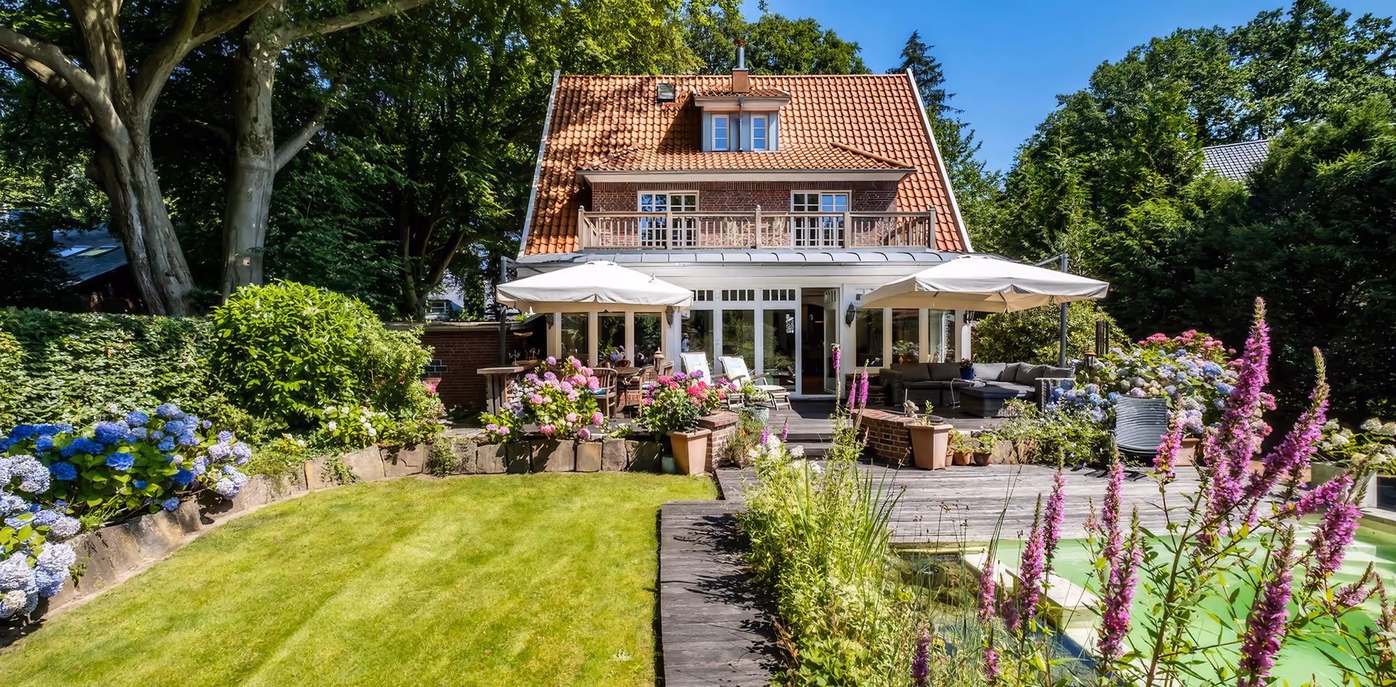 Modernes Einfamilienhaus mit Garage, Garten, Terrasse mit Möbeln und blauem Himmel.