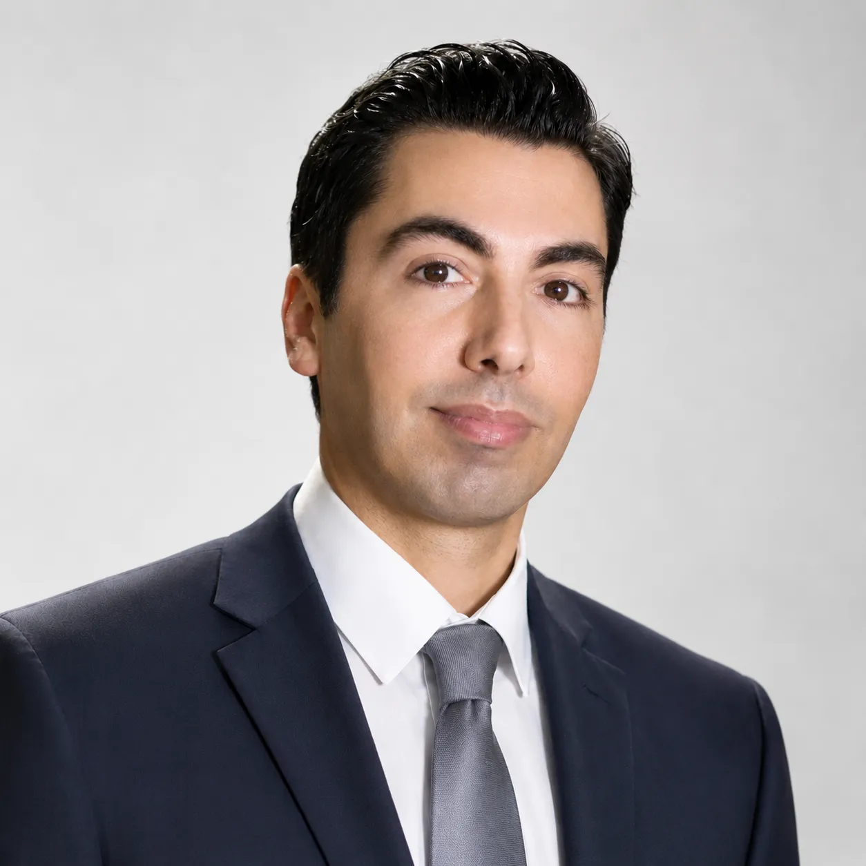 Portrait of man in dark suit, white shirt, and gray tie against a light background.