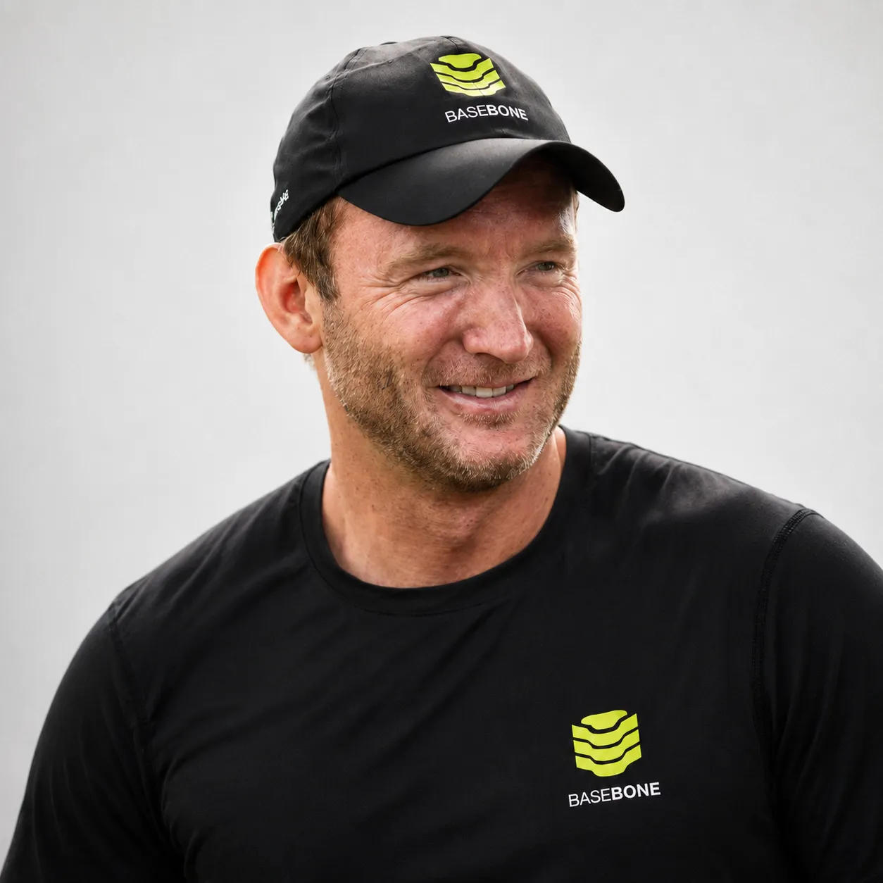 Smiling man wearing a black Basebone cap and t-shirt against a plain light background.